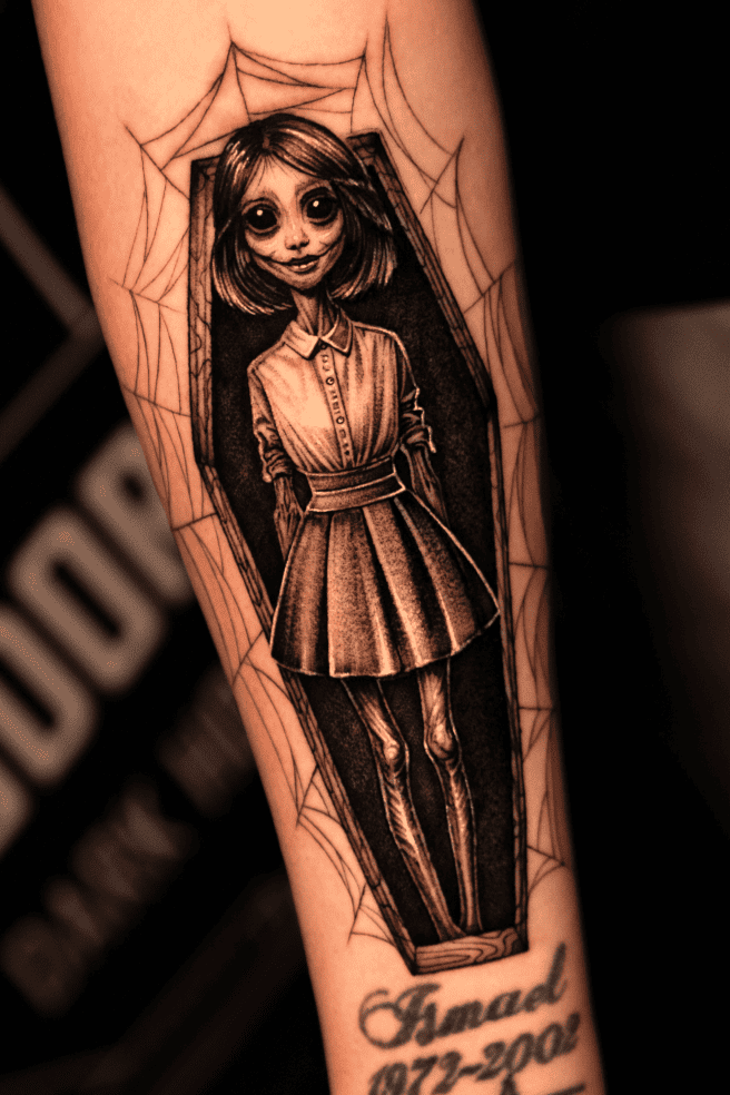 Gothic cartoon girl standing in a coffin surrounded by a spider web, forearm tattoo