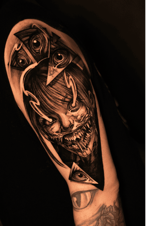 Horned demon with bared teeth and geometric eye panels, black and grey realism shoulder tattoo