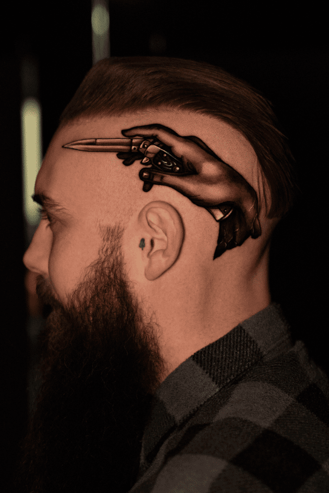 Skeletal hand gripping a dagger, tattooed on the side of the head above the ear